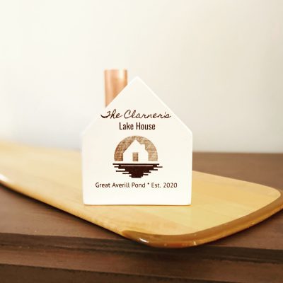 Un petit bougeoir en bois blanc avec une cheminée en cuivre, une image décorative gravée sur mesure et les mots "Lake House, Great Averill Pond, Est 2020".